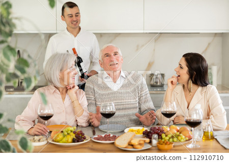 Senior parents and young couple sitting at table drinking wine and having conversation 112910710