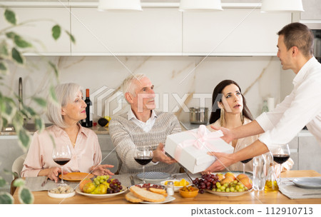 Caring son-in-law surprising father-in-law with present during family feast Caring son-in-law surprising father-in-law with present during family feast 112910713