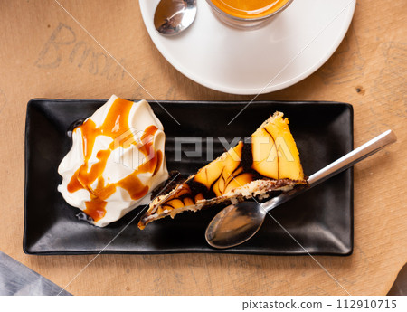 On black plate is thin slice of cheesecake with ball of ice cream with caramel sauce 112910715