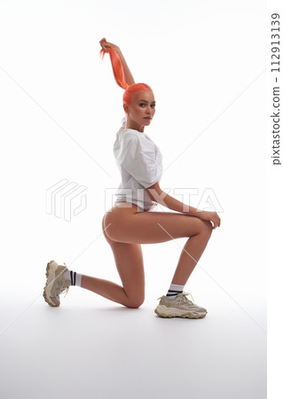 Slim woman in panties and t-shirt in the lunge sitting on floor in studio 112913139