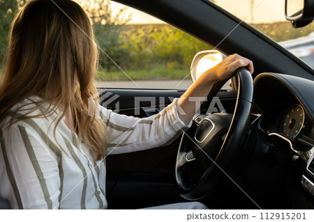 Young woman parking while driving car on highway road during sunset. Womandriver looking for help. Business woman busy driving Young woman parking while driving car on highway road during sunset. Womandriver looking for help. Business woman busy driving 112915201