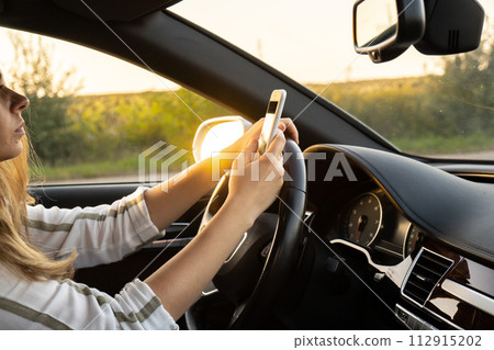 Woman sending messages with smartphone while driving automobile. Female driver using mobile phone on the road during driving the car. Safety and technology 112915202