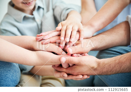 Close-up of several hands placed on top of one another in stack. Big family putting stacked hands together promising work in team. All family members showing their support to each other. Close-up of several hands placed on top of one another in stack. Big family putting stacked hands together promising work in team. All family members showing their support to each other. 112915685