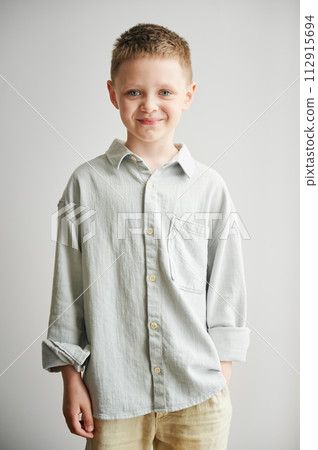 Portrait of happy boy in casual clothes keeping hand in pocket. Adorable boy smiling to camera. Stylish kid posing on white background. 112915694