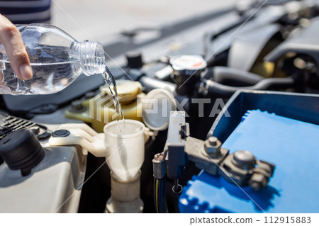 Close up,Pouring clean water from plastic bottle into the windshield washer fluid tank of a car,filling the windshield washer fluid,check liquid level in engine room,service and maintenance concept Close up,Pouring clean water from plastic bottle into the windshield washer fluid tank of a car,filling the windshield washer fluid,check liquid level in engine room,service and maintenance concept 112915883