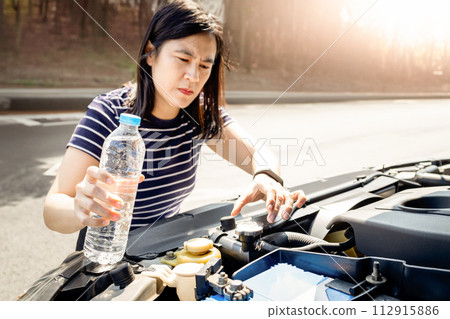 Asian woman check the radiator system and fluid level in the car radiator is too low after engine overheated,she uses water instead of coolant while traveling,outdoor emergency on the side of the road 112915886