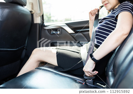 Happy smiling woman wearing safety belt,prevent injury or loss,sit in the back seat of a car,fastening her seat belt for safety in a motor vehicle before traveling on the road,safe from harm or injury 112915892