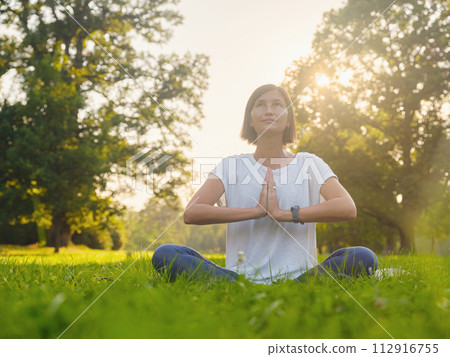 Young asian woman doing meditation in morning or evening at park, healthy woman relaxing and practicing yoga at city park. Mindfulness, destress, Healthy habits and balance concept 112916755