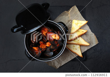 Fresh mussels in a black saucepan in tomato sauce. Seafood dish. White bread crackers. Top view. Fresh mussels in a black saucepan in tomato sauce. Seafood dish. White bread crackers. Top view. 112916911