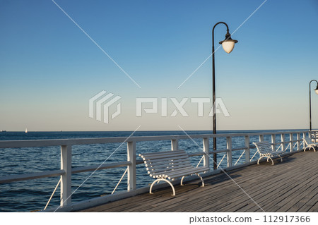 White Old wood bridge pier against beautiful sunset sky natural background, backdrop wallpaper multipurpose sea scene. White benches no people in Gdynia Orlowo, Poland. Wooden pier, molo with marina 112917366