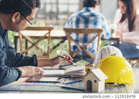 Civil construction engineer working with laptop at desk office with white yellow safety hard hat at office on construction site. Asian young man architecture project manager sitting at office on site Civil construction engineer working with laptop at desk office with white yellow safety hard hat at office on construction site. Asian young man architecture project manager sitting at office on site 112918436