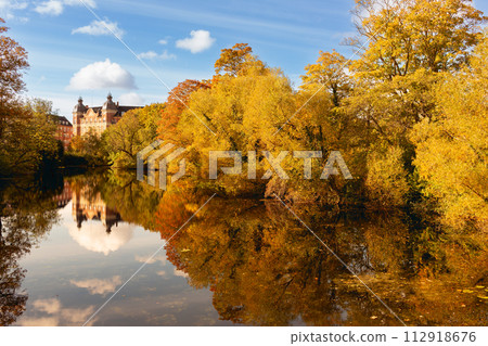 Trees in autumn reflected in the river. In warm yellow and orange colors Trees in autumn reflected in the river. In warm yellow and orange colors 112918676