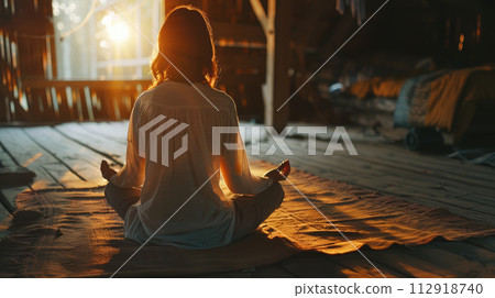 Woman meditating in a rustic cozy room. Back view. Yoga lotus pose. 112918740