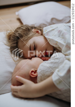 Portrait of big sister cuddling newborn, little baby. Girl lying with her new sibling in bed. Sisterly love, joy for new family member. Portrait of big sister cuddling newborn, little baby. Girl lying with her new sibling in bed. Sisterly love, joy for new family member. 112919412