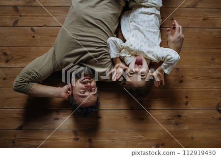 Top view of father with daughter lying on floor laughing together. Girls dad. Unconditional paternal love, Father's Day concept. Top view of father with daughter lying on floor laughing together. Girls dad. Unconditional paternal love, Father's Day concept. 112919430