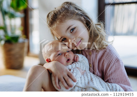 Portrait of big sister holding newborn sister. Girl carefully cuddling small baby. Sisterly love, joy for new family member. Portrait of big sister holding newborn sister. Girl carefully cuddling small baby. Sisterly love, joy for new family member. 112919455
