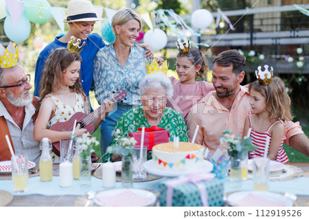 Garden birthday party for senior lady. Beautiful senior birthday woman receiving gift from family. 112919526