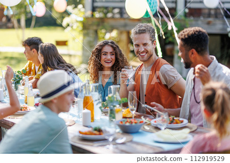 Portrait of couple sitting at the table with family and friends at the family garden party. 112919529