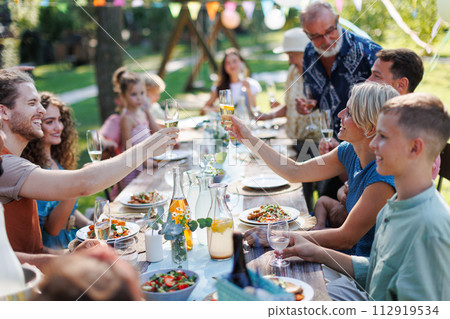 Family clinking glasses at summer garden party. Celebratory toast at the table. Family clinking glasses at summer garden party. Celebratory toast at the table. 112919534