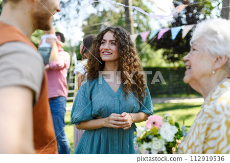 Grandparents giving flowers and present to granddaughter as surprise at birthday party. Friends and family reunite at garden party after a long time apart. 112919536