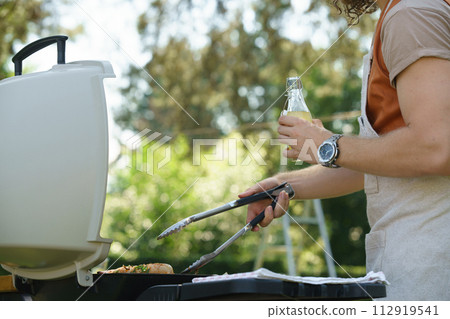 Man grilling on outdoor grill and drinkig lemonade. Outdoor grill or BBQ party in the garden. 112919541