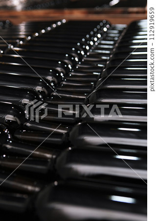 Wine bottles are stacked for storage. The bottles are in rows. New wine. A small winery. Selective focus. Vertical photo. 112919659