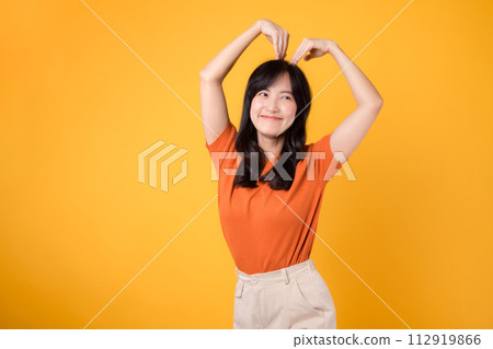 Warmth and authenticity shine through as a cheerful Asian woman in her 30s embraces love with a heart-shaped gesture and an infectious smile. Warmth and authenticity shine through as a cheerful Asian woman in her 30s embraces love with a heart-shaped gesture and an infectious smile. 112919866
