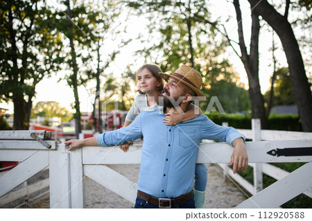Portrait of farmer family, father and young daughter standing on wooden fence on family farm. Concept of multigenerational farming. 112920588