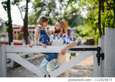 Farmer family, father with daughter sitting on wooden fence on family farm. Concept of multigenerational farming. 112920673