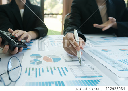 A man is pointing at a graph on a table while another man looks on 112922684