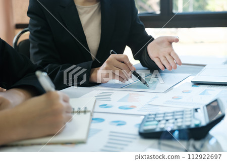 Two women in business suits are discussing a report on a table 112922697