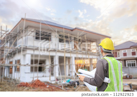 young professional engineer in protective helmet and blueprints paper at the house building construction site 112922923