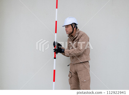 A field worker stands up a surveying pole and checks the direction. A field worker stands up a surveying pole and checks the direction. 112922941