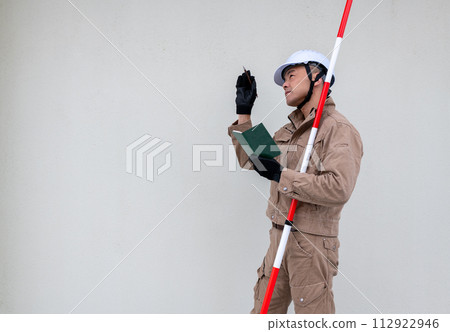 A field worker taking notes while holding a surveying pole under his arm. A field worker taking notes while holding a surveying pole under his arm. 112922946