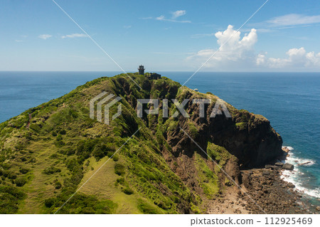 Aerial view of old lighthouse on a cape against the backdrop of the ocean and blue sky. Cape Engano. Palaui Island. Santa Ana Philippines. Aerial view of old lighthouse on a cape against the backdrop of the ocean and blue sky. Cape Engano. Palaui Island. Santa Ana Philippines. 112925469
