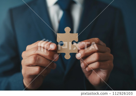 Close-up of Businessman's Hand Holding a Single Puzzle Piece on Blue Background Close-up of Businessman's Hand Holding a Single Puzzle Piece on Blue Background 112926103