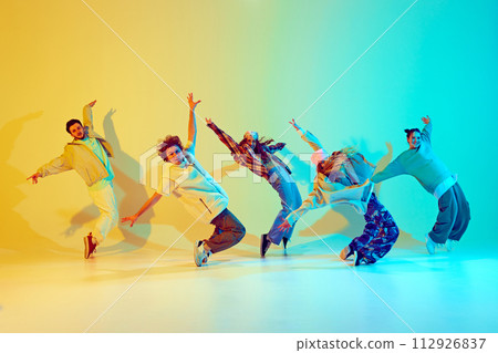 Dynamic performance of five talented dancers in motion, dancing modern dance against gradient green yellow background in neon light. 112926837
