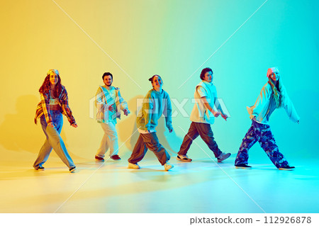 Young people, men and women in dynamic poses dancing hip hop, contemporary dance against gradient green yellow background in neon light Young people, men and women in dynamic poses dancing hip hop, contemporary dance against gradient green yellow background in neon light 112926878