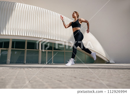 Active woman athlete is jogging in morning on modern building background. Healthy life concept Active woman athlete is jogging in morning on modern building background. Healthy life concept 112926994
