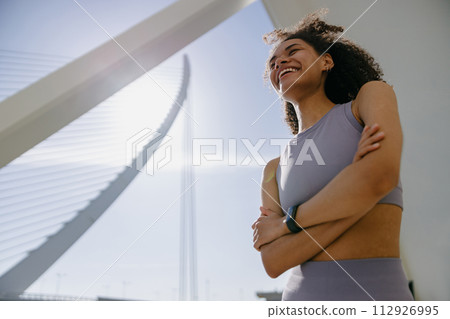 Woman in tracksuit have rest after workout standing with crossed hands on building background 112926995