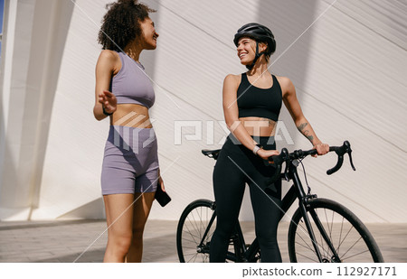 Young sporty female friends talking while standing in city before training. High quality photo Young sporty female friends talking while standing in city before training. High quality photo 112927171