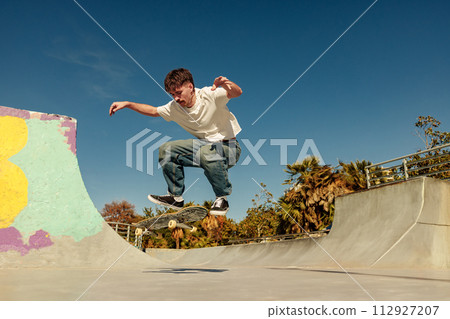A young man doing tricks on his skateboard at the skate park. Active sport concept 112927207