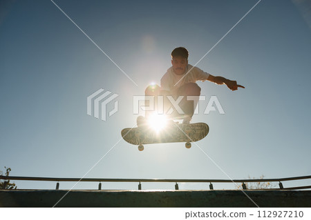 A young man doing tricks in the air on his skateboard at the skate park. Active sport concept A young man doing tricks in the air on his skateboard at the skate park. Active sport concept 112927210