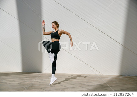 Female athlete in sportswear leaping in air with wall backdrop outdoors. Healthy lifestyle concept Female athlete in sportswear leaping in air with wall backdrop outdoors. Healthy lifestyle concept 112927264