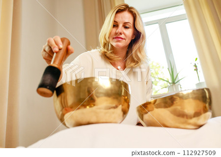 Woman playing on a tibetian singing bowl in cozy room meditating in a yoga Woman playing on a tibetian singing bowl in cozy room meditating in a yoga 112927509