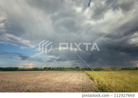 A rainbow in the cloudy sky over the rural fields 112927668