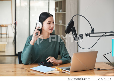 A woman is sitting at a desk with a laptop and a microphone 112928283