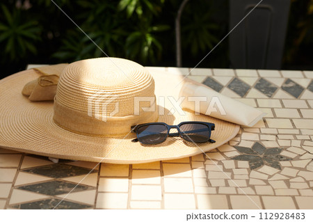 Sunglasses and straw hat on tiled floor by swimming pool 112928483