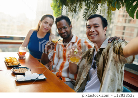 Smiling Vietnamese man taking selfie with best friends in bar 112928522