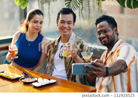 Cheerful man photographing with best friends in rooftop bar 112928525